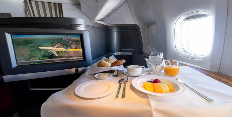 سرو صبحانه در Cathay Pacific First Class با میز بزرگ، مانیتور عریض و پنجرههای روشن هواپیما.