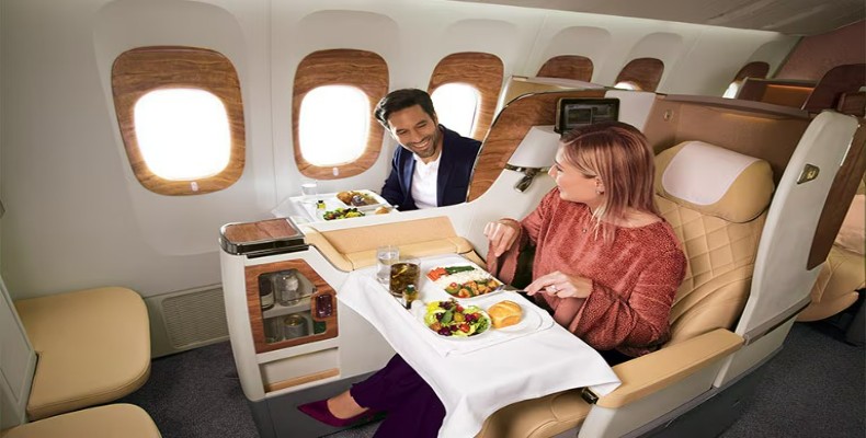 مسافران در حال صرف غذای لوکس در Emirates Business Class با صندلیهای بزرگ و طراحی داخلی طلایی.