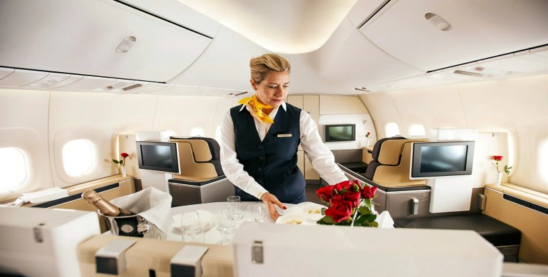 مهماندار در حال سرویسدهی در Lufthansa First Class با صندلیهای پهن و فضای لوکس کابین.