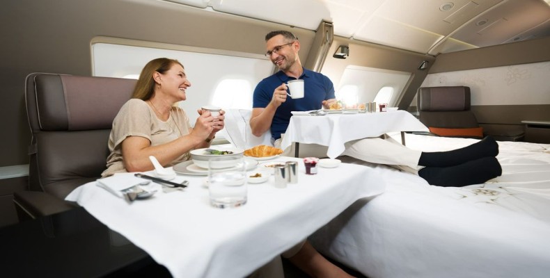 زوجی در حال صرف غذا در Singapore Airlines First Class Suites با تخت دونفره و سرویس غذایی سطحبالا.
