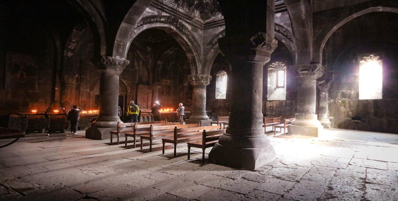 فضای داخلی کلیسای گغارت با ستونهای سنگی و شمعهای روشن زائران