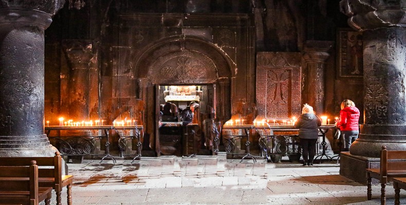 فضای داخلی کلیسای گغارت با ستونهای سنگی و شمعهای روشن زائران