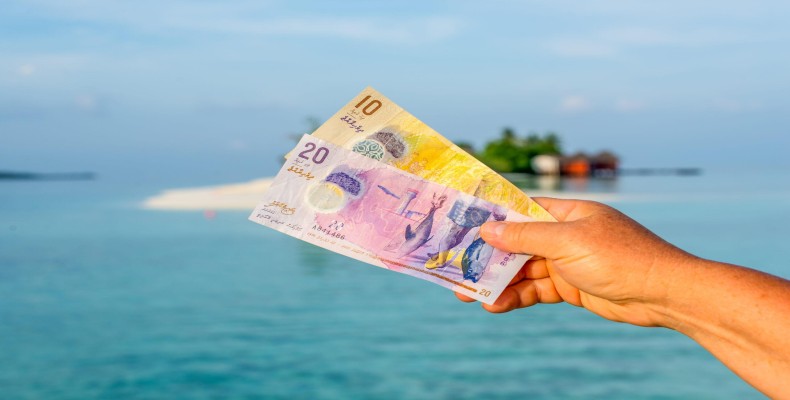 واحد پول مالدیو در دست گردشگر با پسزمینه جزیرههای مرجانی