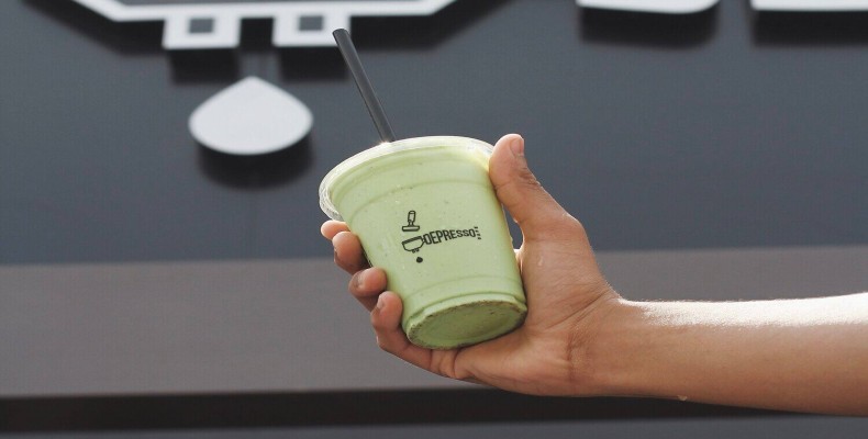 نوشیدنی سرد سبز رنگ در کافه دپرسو دبی با لوگوی خاص روی لیوان