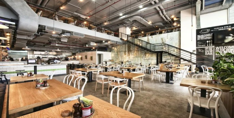 فضای بزرگ و صنعتی کافه تام اند سرج در القوز دبی با میزهای چوبی و طراحی باز دو طبقه