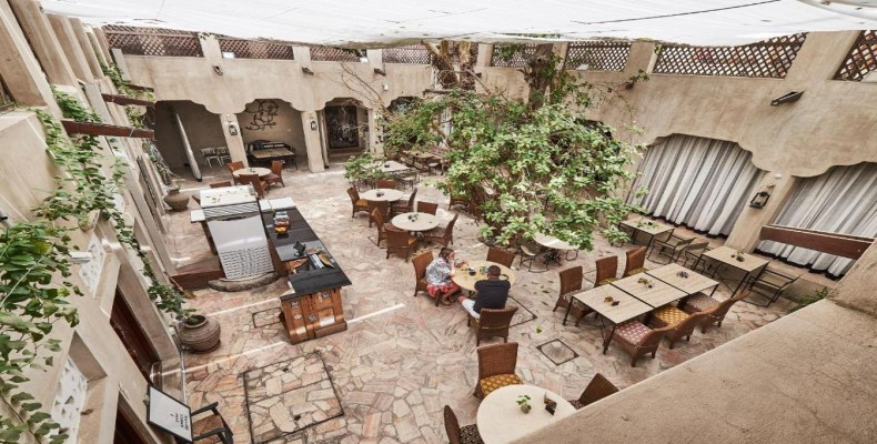 حیاط سنتی و آرام کافه ایکس وی ای در محله تاریخی الفهیدی دبی با درخت مرکزی و میزهای سنگی