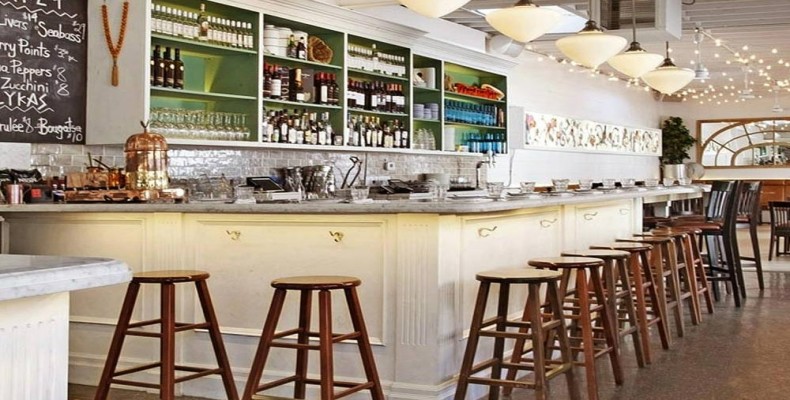 فضای روشن و سفید رستوران Mamakas Taverna تورنتو با دکور یونانی و صندلیهای چوبی