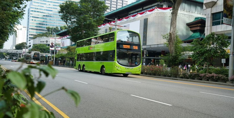 اتوبوس دوطبقه سبز در خیابان‌های سنگاپور در کنار ساختمان‌های تجاری